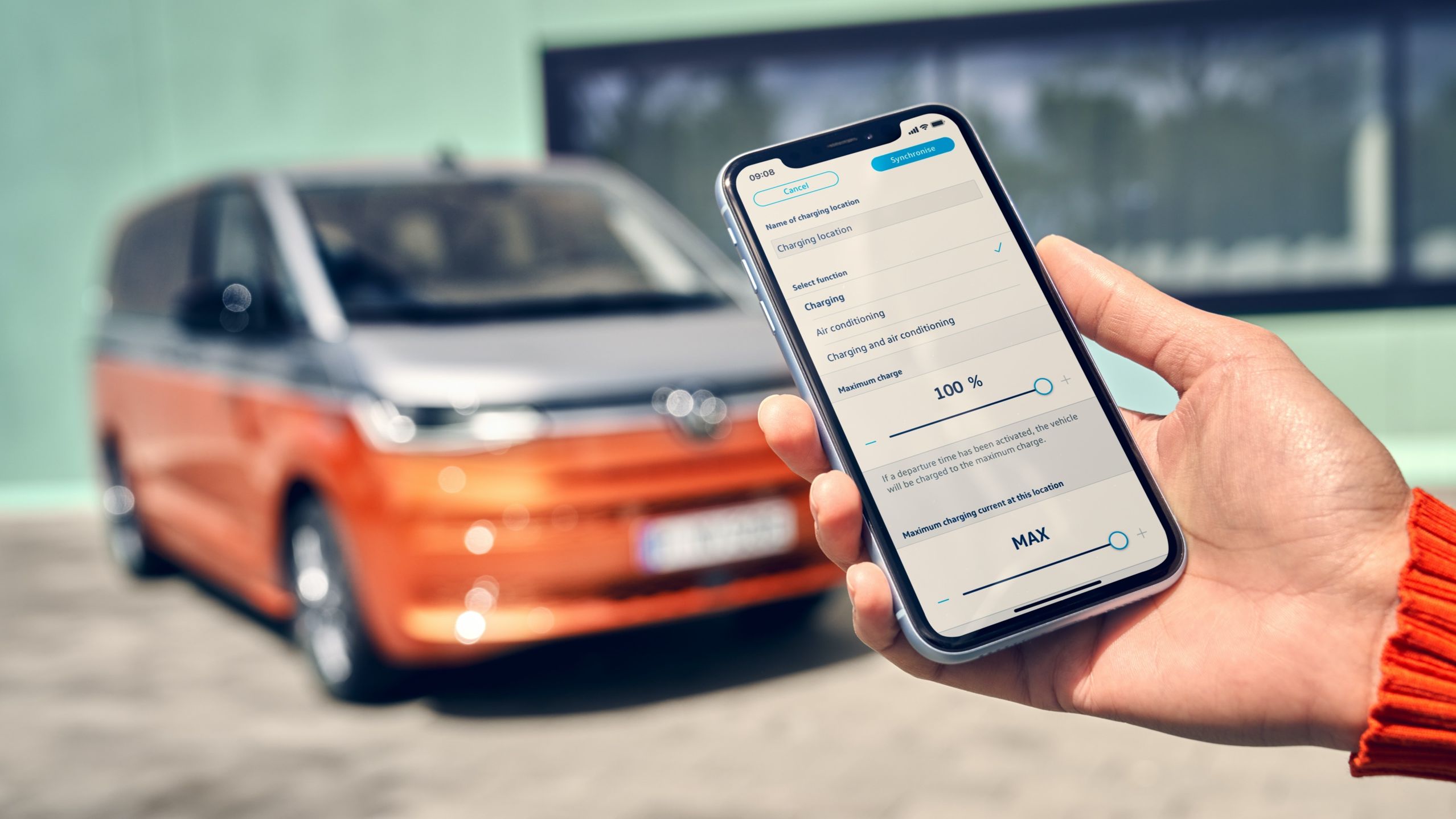 Eine Hand hält ein Smartphone. Im Hintergrund sieht man den VW Multivan Energetic T7 2021 verschwommen. 