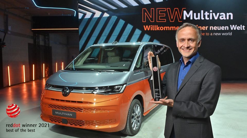 Eine Hand hält ein Smartphone. Im Hintergrund sieht man den VW Multivan Energetic T7 2021 verschwommen. 