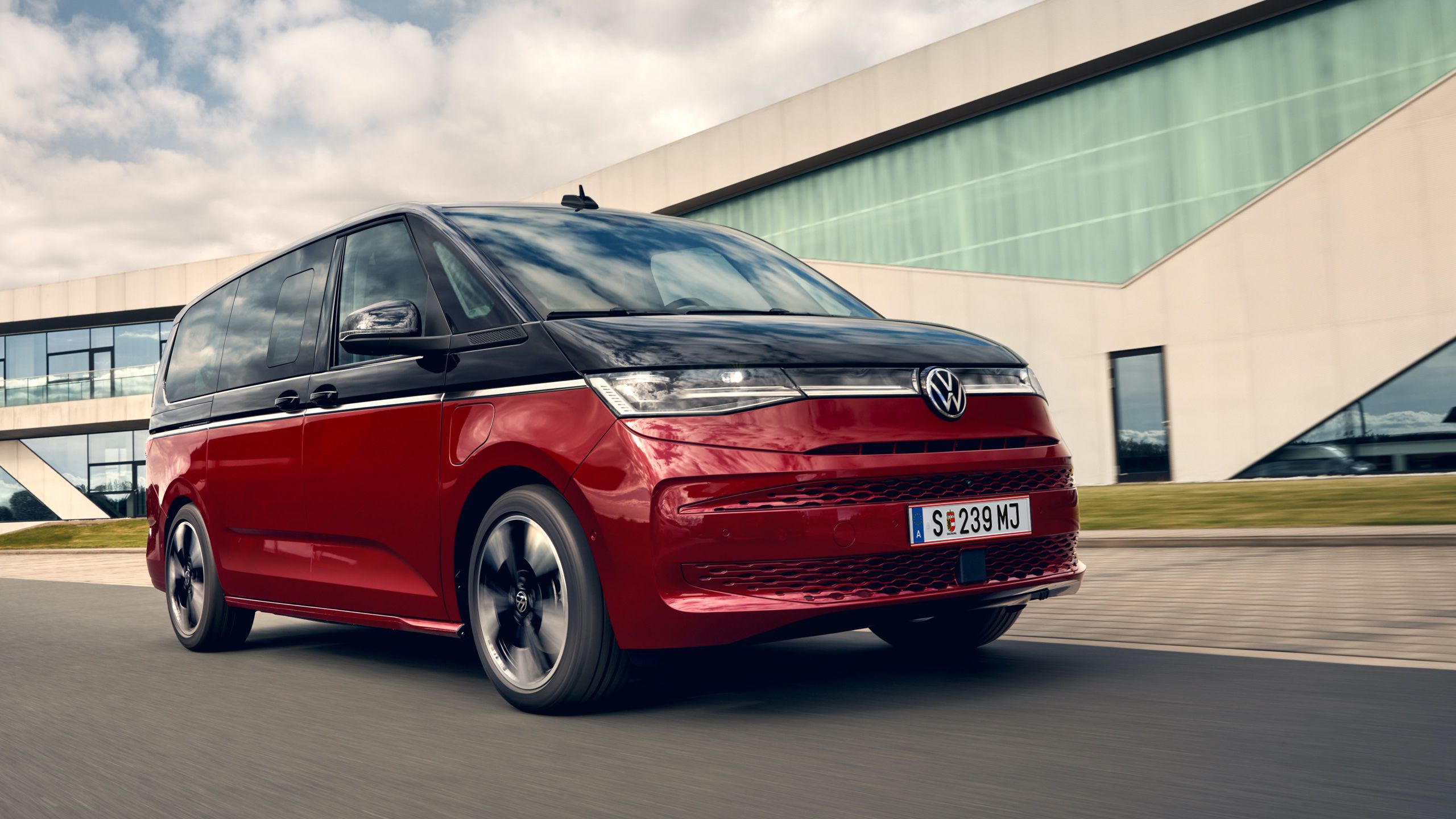 Der VW Multivan Style T7 2021 vor einem Gebäude aus Glas. 