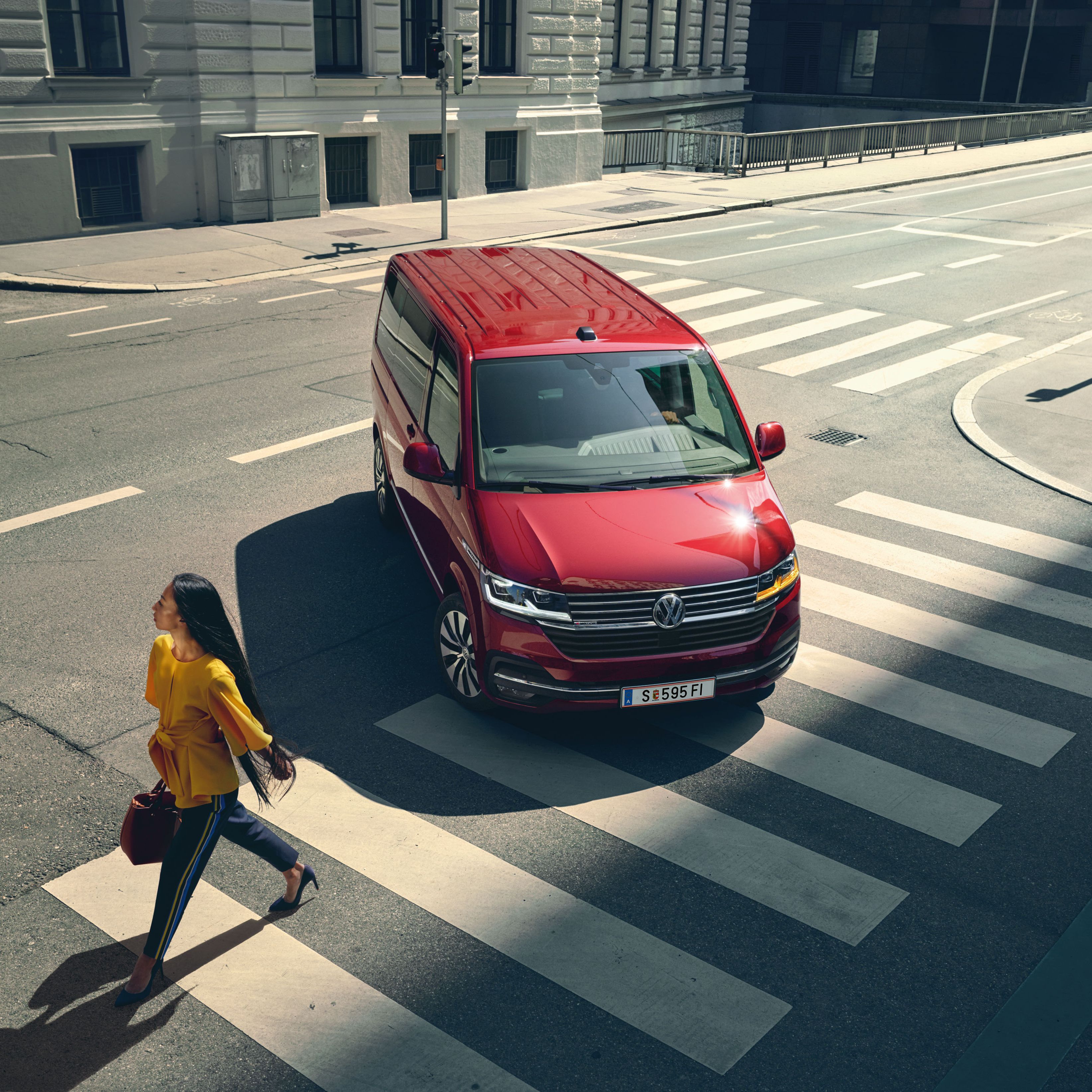 VW Multivan 6.1 fährt vor einem Schutzweg. Eine Frau mit gelben Oberteil überquert den Schutzweg.